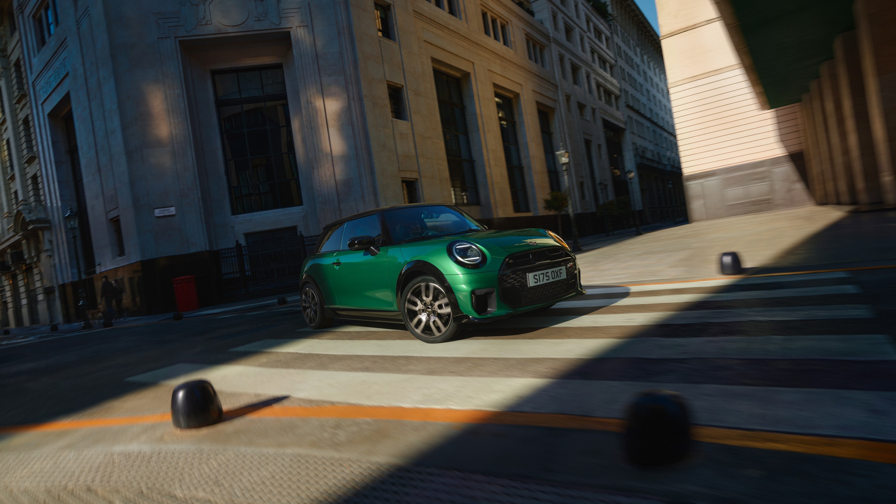 Eine Person geht über eine verschneite Fläche auf einen schwarzen MINI Cooper zu, der vor einer winterlichen Berglandschaft steht.